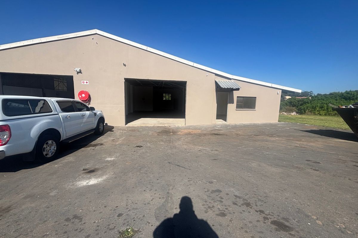 Exterior view of an industrial warehouse building featuring a large roller door entrance, concrete apron, and asphalt driveway area.