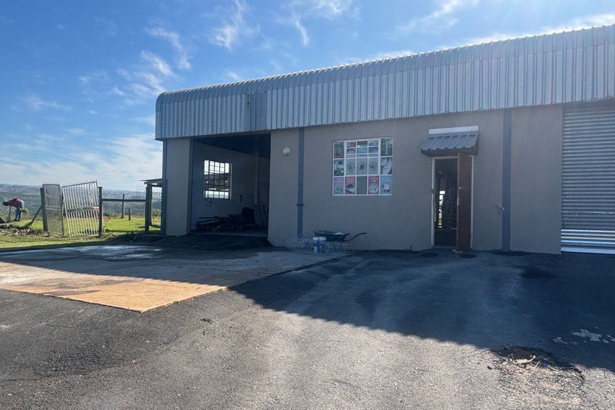Industrial property exterior featuring a corrugated metal roof, roller shutter door, and asphalt driveway with a metal security gate.