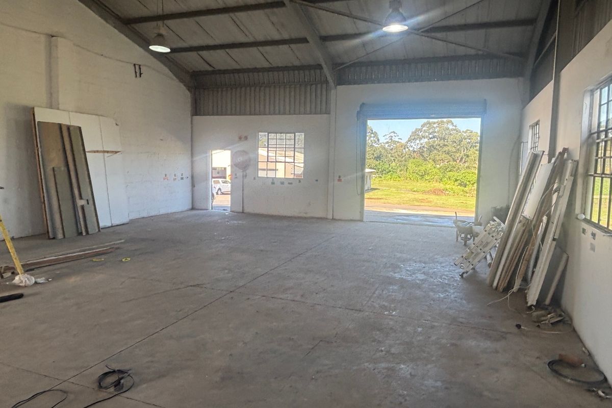 Spacious industrial utility area featuring exposed steel roof trusses, concrete flooring, and a large roller shutter door providing access to the exterior.