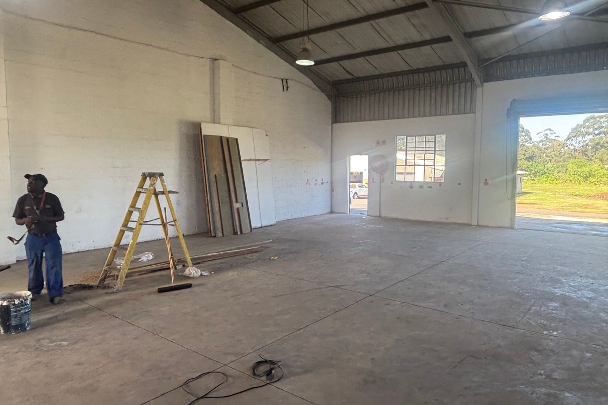Spacious industrial warehouse unit featuring high ceilings with exposed steel trusses, concrete flooring, and large roller shutter access.