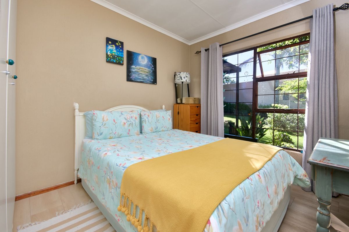 A bright bedroom featuring laminate flooring, a built-in wardrobe, and a large window overlooking the garden, providing ample natural light.