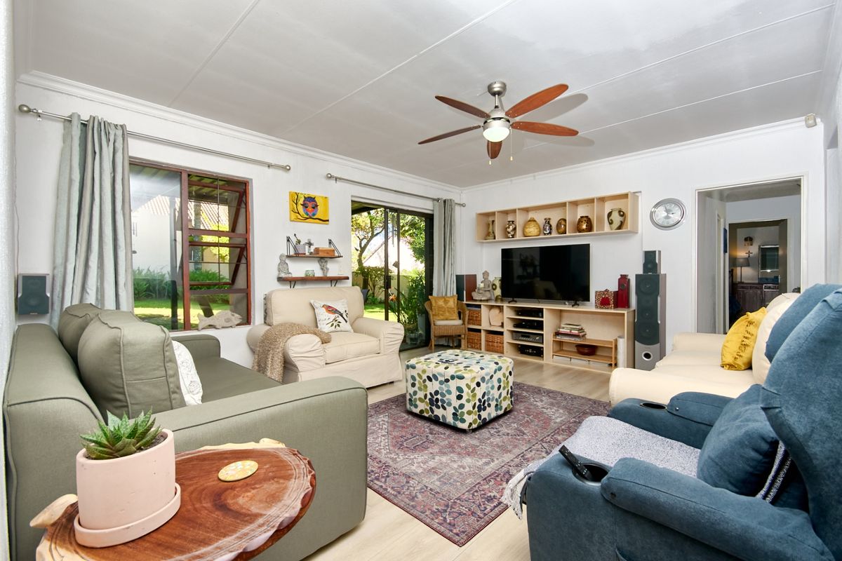 A comfortable living room featuring laminate flooring, a ceiling fan, and large sliding glass doors that provide natural light and access to the garden.