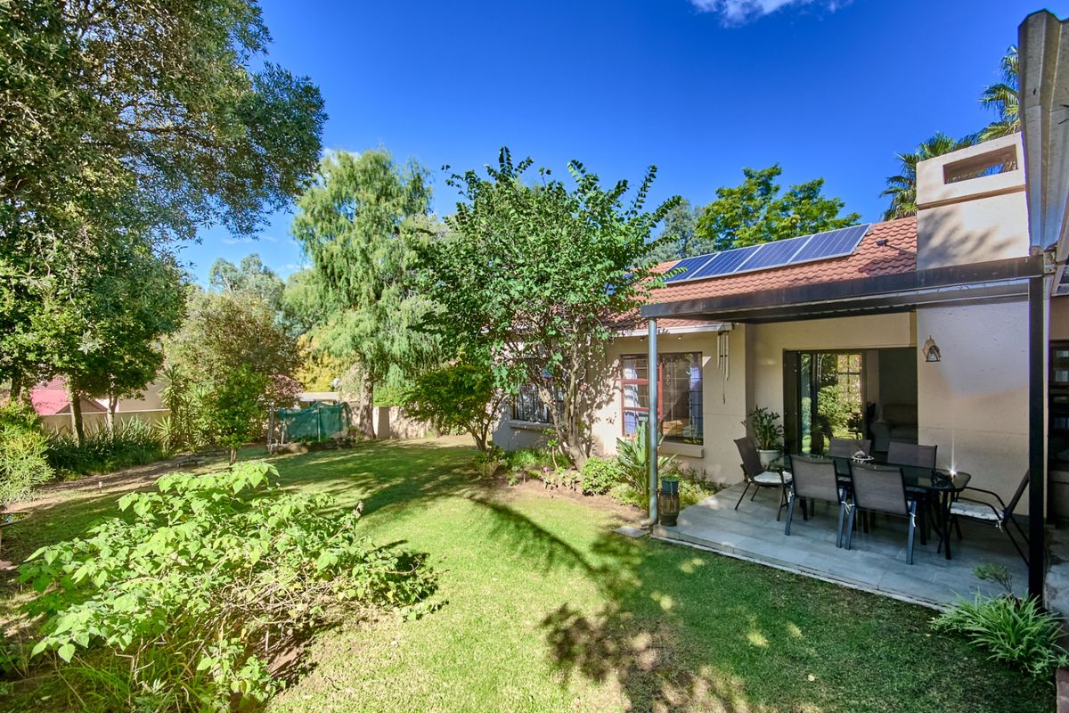 Rear view of the property featuring a covered patio, landscaped garden, and roof-mounted solar panels.