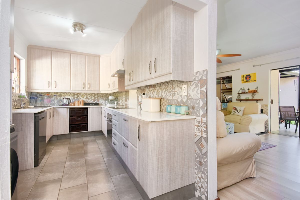 A functional kitchen featuring light-toned built-in cabinetry, patterned tiled splashbacks, integrated appliances, and durable floor tiles, seamlessly connecting to the adjacent living area.