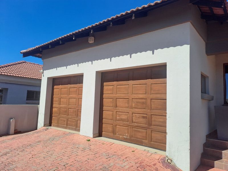 A double garage with wooden panel doors, tiled roof, and paved driveway access.