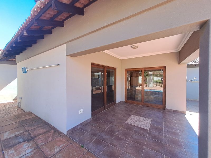 A covered outdoor patio area featuring tiled flooring, exposed timber rafters, and sliding glass doors providing access to the interior living space.