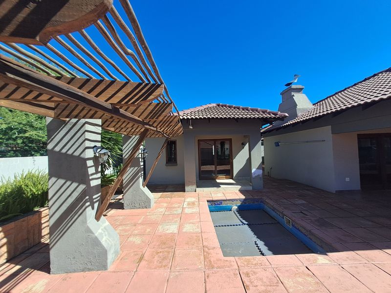 Rear exterior area featuring a tiled patio, a swimming pool with a safety cover, and a wooden pergola structure attached to the home.