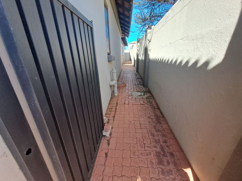 A narrow side passage featuring paved flooring, a metal gate, and high boundary walls.