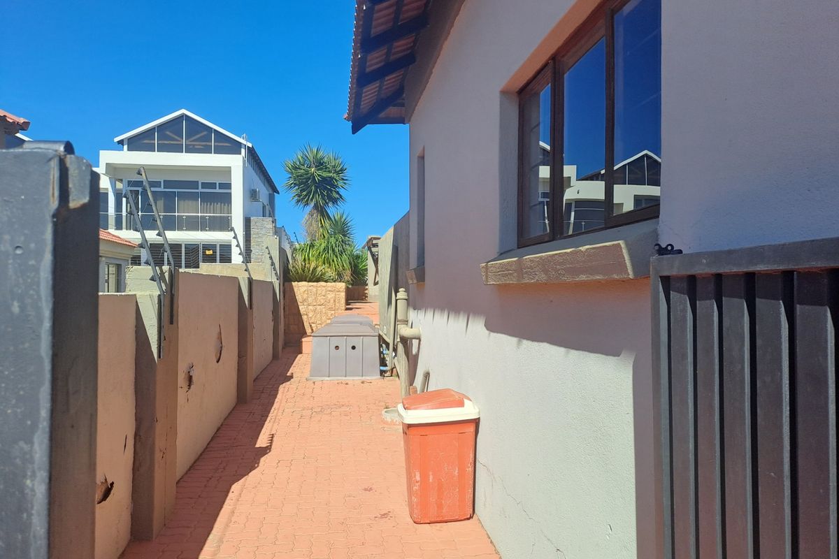 A narrow side passage featuring paved flooring and a boundary wall with visible plaster damage, leading towards the rear of the property.