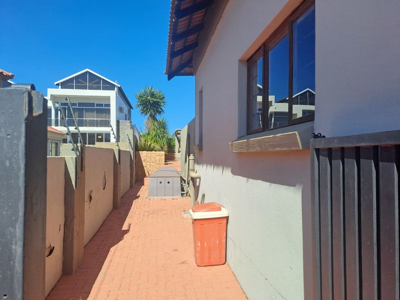 A narrow side passage featuring paved flooring and a boundary wall with visible plaster damage, leading towards the rear of the property.