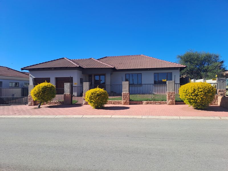 Front elevation of a well-maintained single-story house featuring a tiled roof, double garage, and secure perimeter fencing with stone-clad pillars.