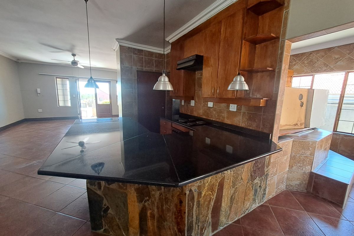 Open-plan kitchen featuring a stone-clad breakfast bar, granite countertops, wooden cabinetry, and tiled flooring, offering a functional layout for renovation.