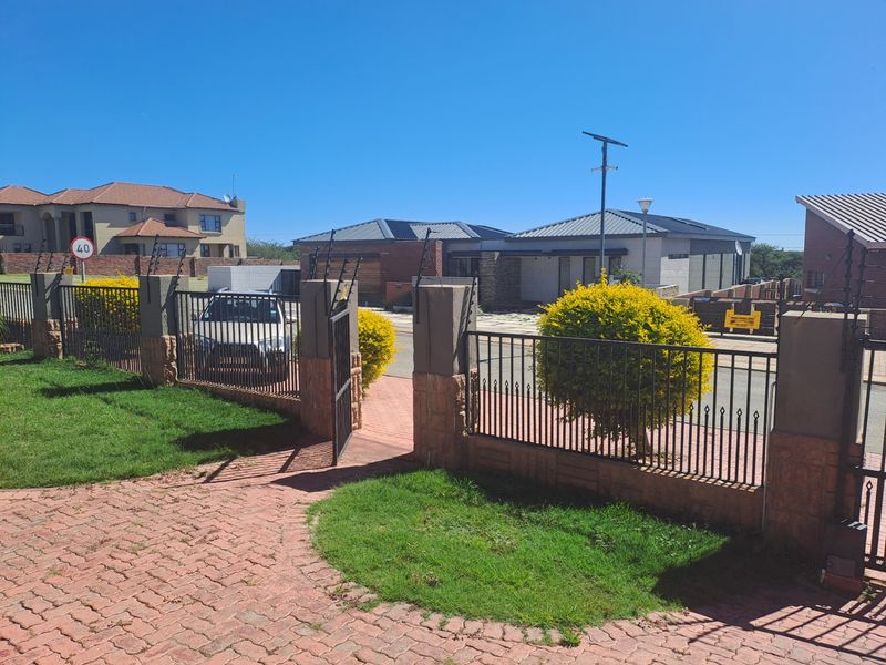 A view of the property entrance featuring a paved driveway, secure metal gate, and perimeter wall with electric fencing in a residential estate.