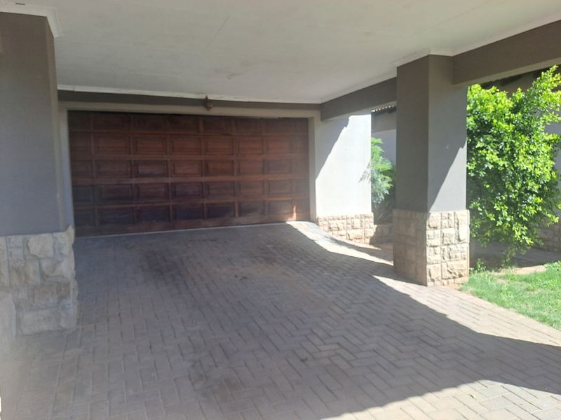 A covered carport area featuring a wooden garage door, stone-clad pillars, and a paved driveway.