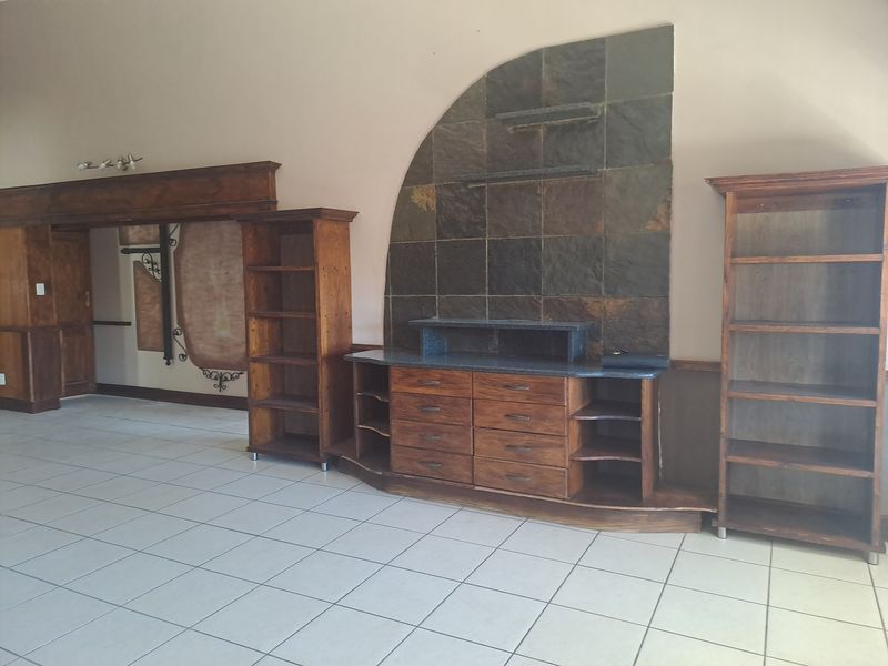 Spacious living area featuring built-in wooden cabinetry, a stone tile feature wall, and neutral ceramic floor tiles throughout.