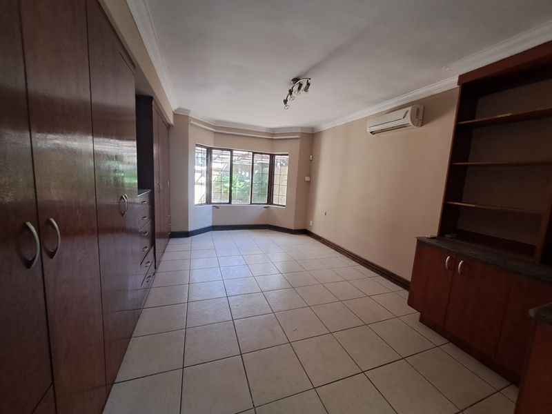 Spacious bedroom featuring extensive built-in cabinetry, tiled flooring, a bay window, and a wall-mounted air conditioning unit.