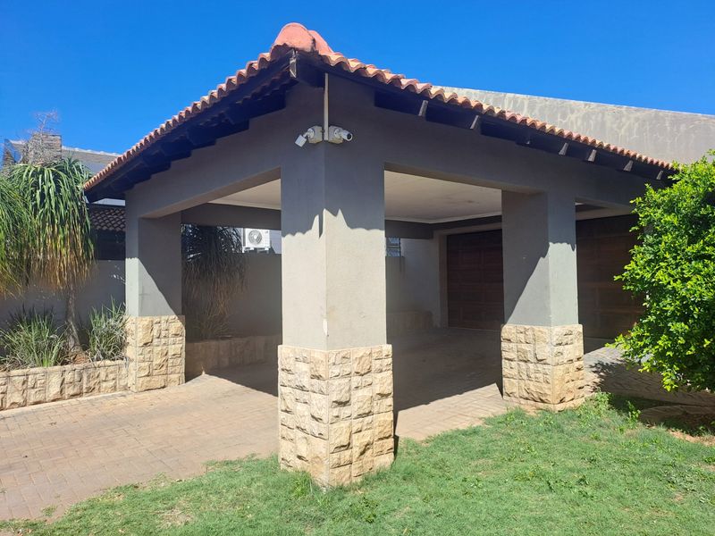 A covered carport area featuring stone-clad pillars, a tiled roof, and paved driveway access to the main garage structure.