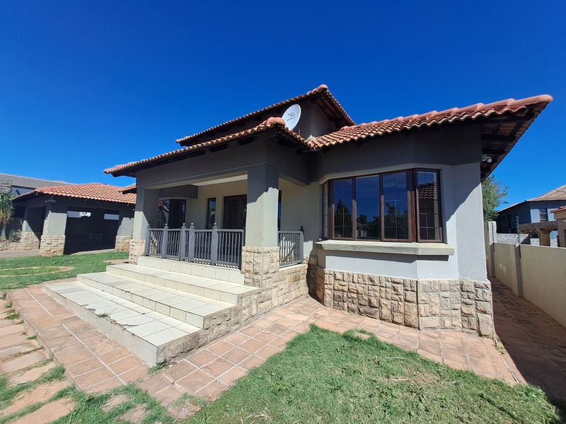 Front elevation of a house featuring a covered patio, stone cladding accents, tiled entrance steps, and a bay window under a terracotta tiled roof.