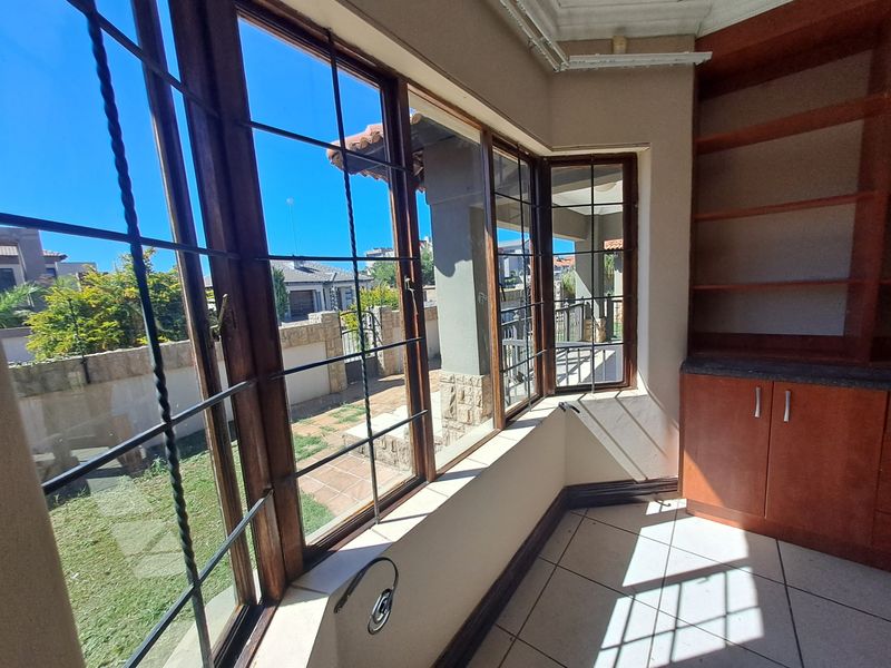 Bright living area featuring large wooden-framed windows with security bars, tiled flooring, and built-in cabinetry, offering a view of the garden.