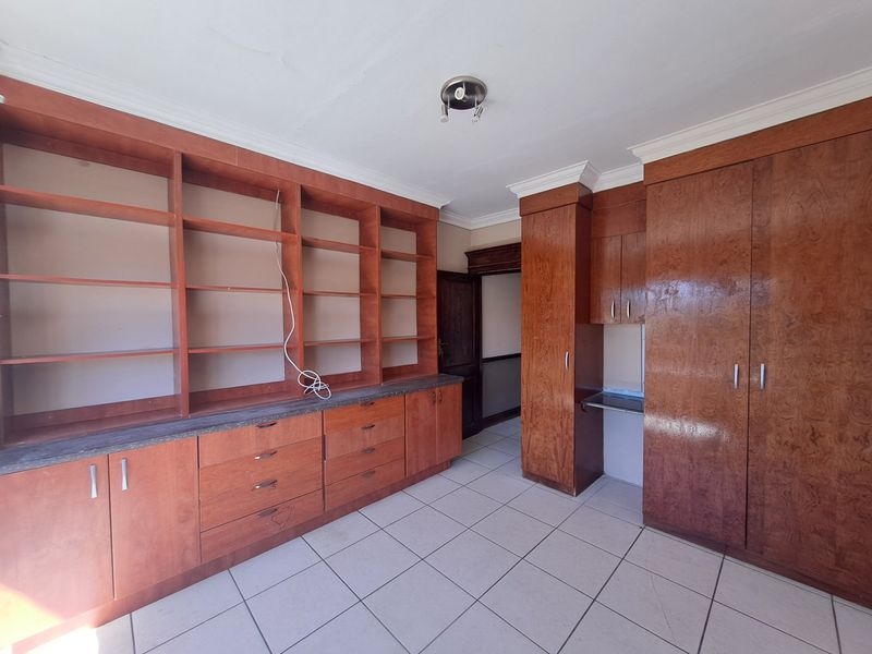 A spacious home office or study featuring extensive built-in wooden cabinetry, shelving, and tiled flooring, offering ample storage and workspace potential.
