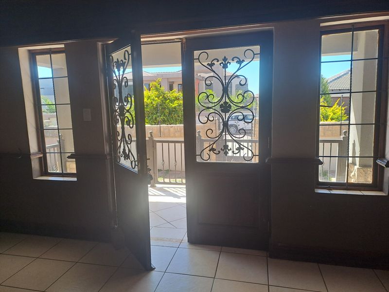 An empty living area featuring tiled flooring, decorative wrought iron security gates, and matching window security bars, opening onto an outdoor patio space.