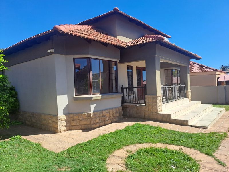 Front elevation of a well-maintained house featuring terracotta roof tiles, stone cladding accents, a covered porch with iron railings, and a paved entrance.