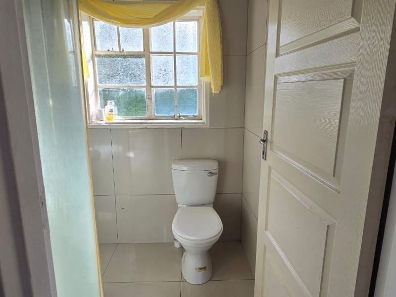 A functional bathroom featuring tiled walls, tiled flooring, and a window, providing a clean and simple space.