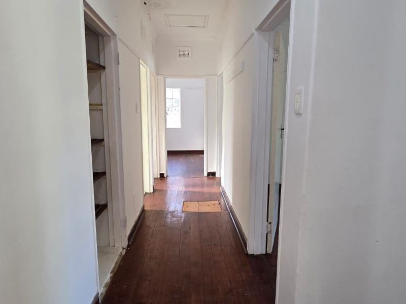A vacant hallway featuring original timber flooring, built-in shelving, and a ceiling access hatch, connecting multiple rooms within the home.
