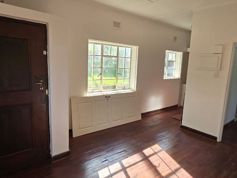 An empty living area featuring original timber flooring, steel-framed windows, and a classic timber entrance door, offering a blank canvas for renovation.