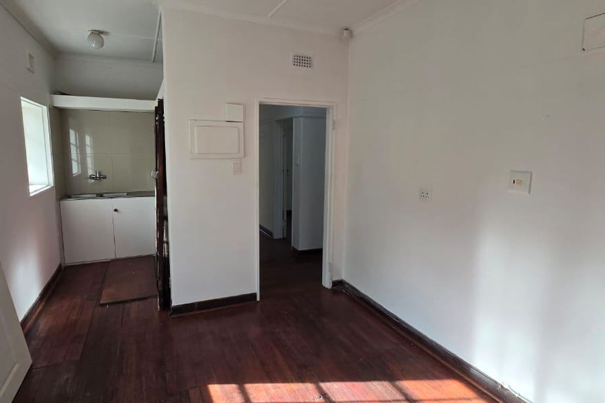 A compact, empty kitchen area featuring timber flooring, a built-in sink with base cabinetry, and a white brick feature wall.