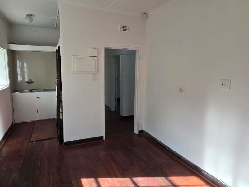 A compact, empty kitchen area featuring timber flooring, a built-in sink with base cabinetry, and a white brick feature wall.