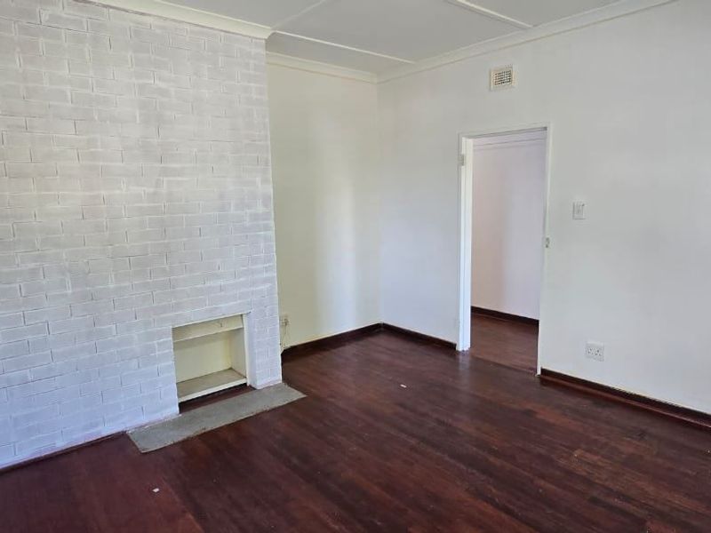 An empty living room featuring original hardwood flooring and a painted brick fireplace, offering a blank canvas for interior design.