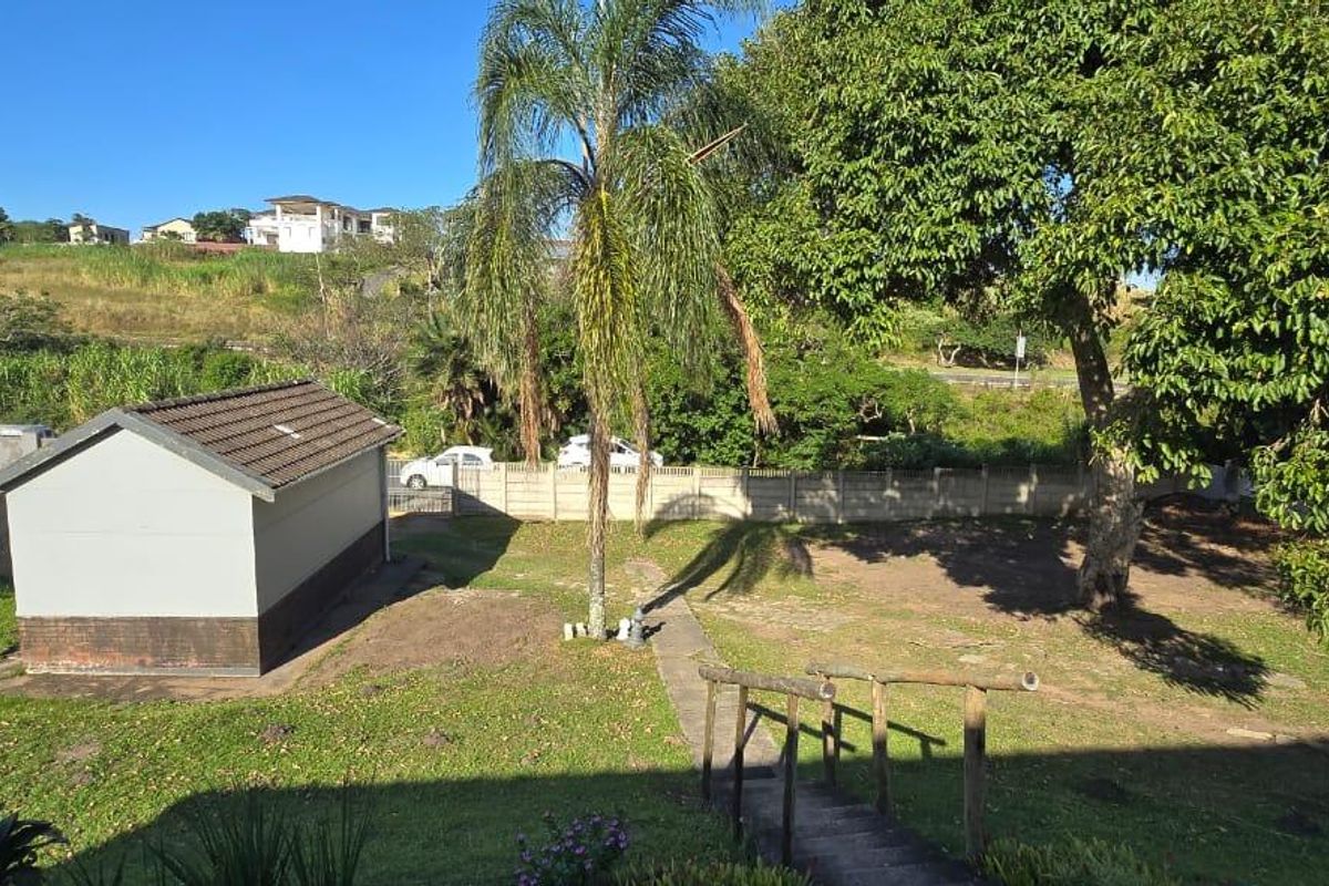 A spacious rear garden area featuring a detached outbuilding, mature trees, and perimeter walling, providing a private outdoor space.