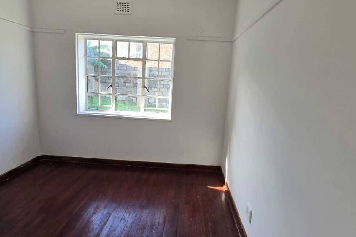 A vacant bedroom featuring polished timber flooring, white walls, and a steel-framed window providing natural light.