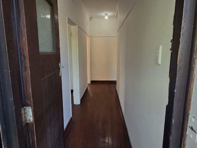 A narrow interior hallway featuring timber flooring and a solid timber entrance door with an integrated security gate.