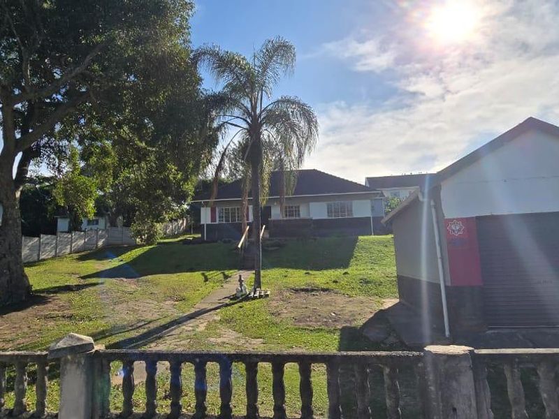 Front view of the property featuring a detached garage, a large lawn area, and a concrete boundary wall.