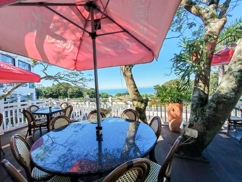 An elevated outdoor patio area featuring timber decking, white balustrade railings, and scenic ocean views, perfect for commercial dining.