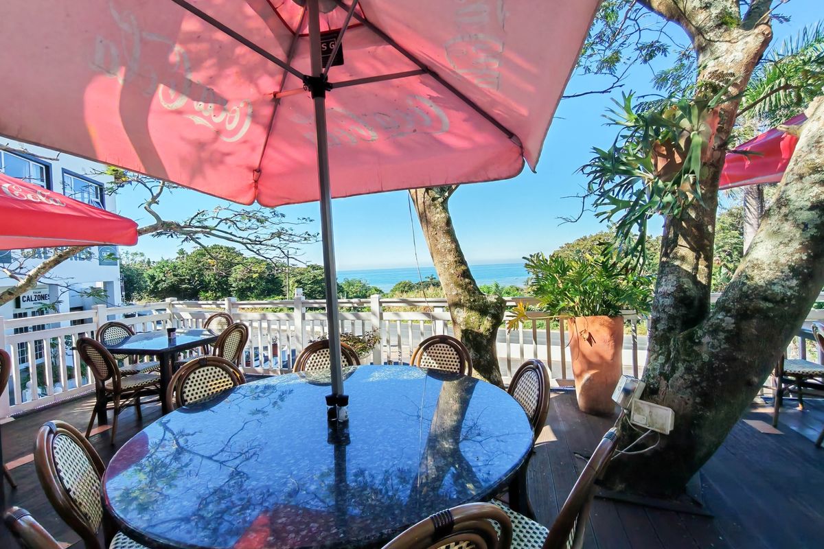An elevated outdoor patio area featuring timber decking, white balustrade railings, and scenic ocean views, perfect for commercial dining.