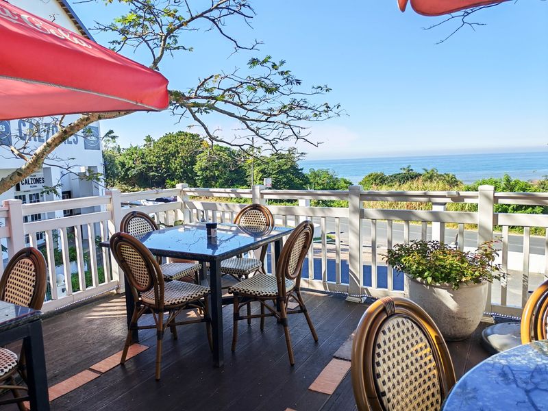An elevated outdoor patio area featuring timber decking and white balustrade railings, offering scenic ocean views and a pleasant dining atmosphere.