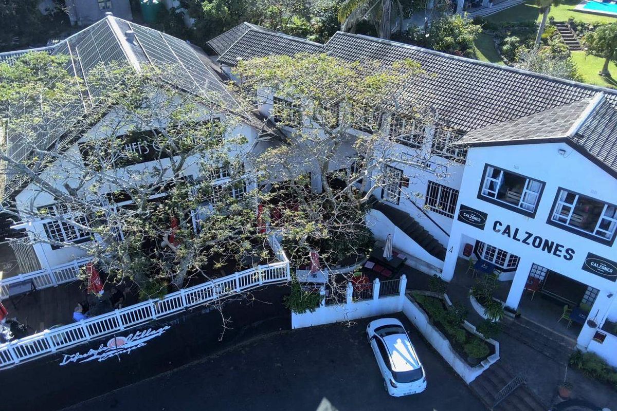 Aerial view of a commercial property complex featuring multiple buildings with tiled roofs, solar panels, an outdoor deck area, and surrounding landscaped grounds.
