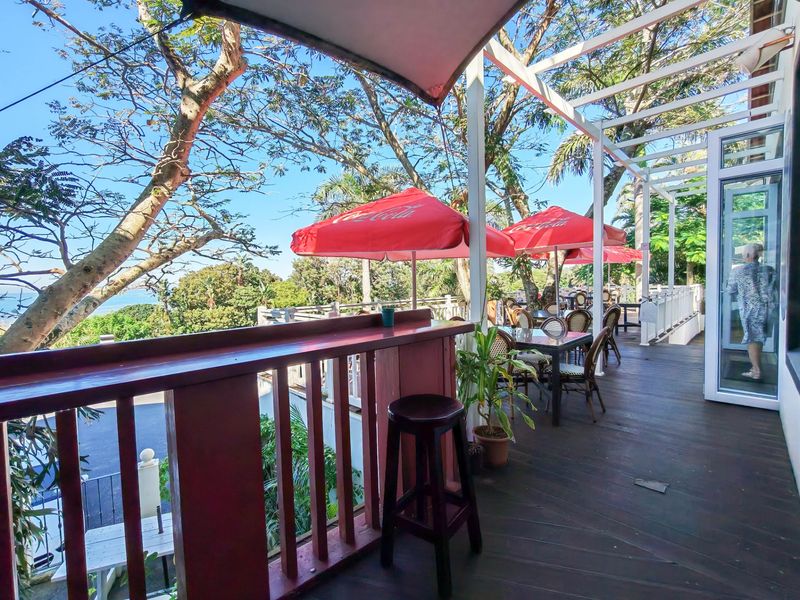An elevated outdoor timber deck featuring a pergola structure, balustrade, and glass door access, offering an open-air seating area with scenic views.