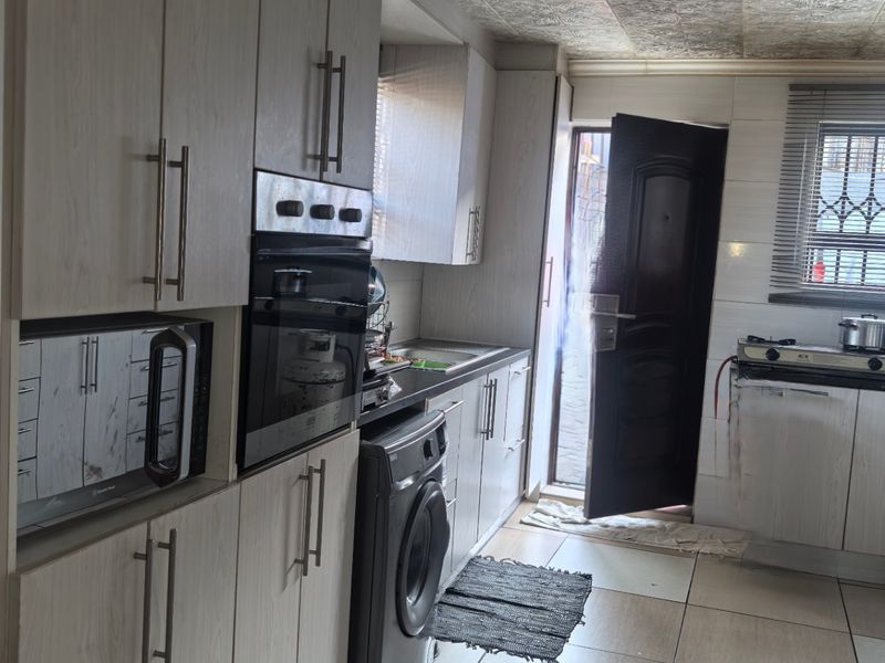 A functional kitchen featuring light wood-grain cabinetry, built-in oven, integrated microwave, and tiled flooring with direct access to the exterior.