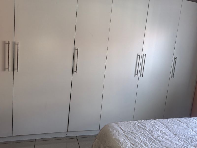 A bedroom featuring floor-to-ceiling built-in white wardrobes with modern metal handles.