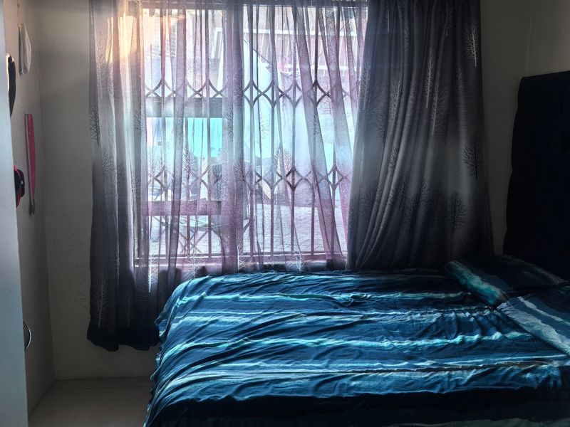 A bedroom featuring tiled flooring and a decorative ceiling, with a window fitted with security bars and curtains.