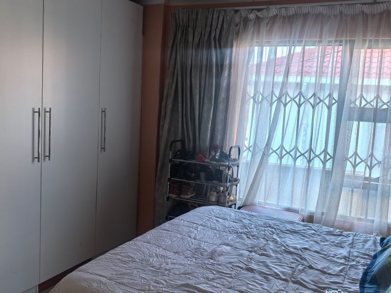A bedroom featuring built-in wardrobes, a window with security gate, and decorative ceiling tiles.