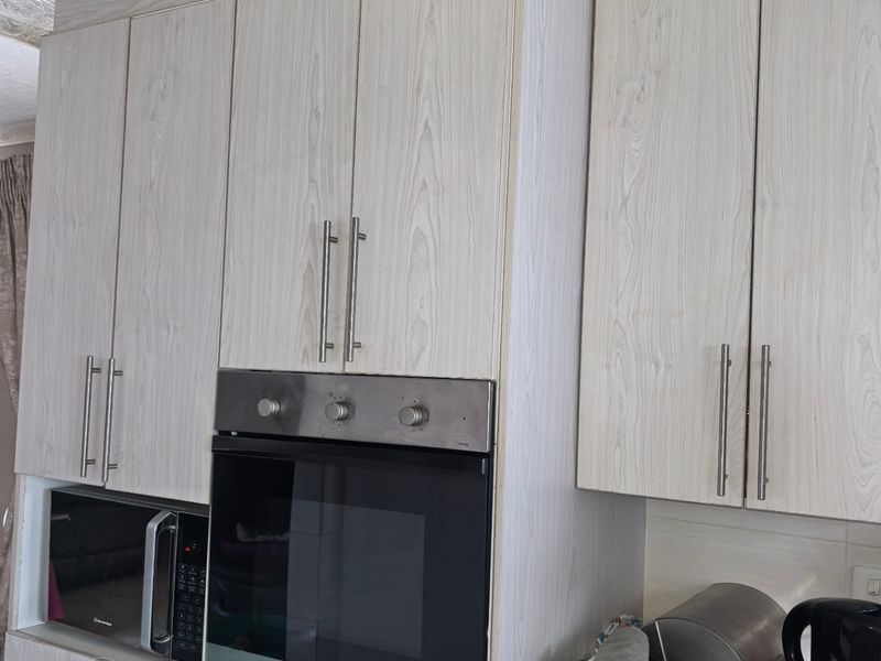 Kitchen cabinetry featuring light wood-grain finish, integrated oven, and built-in microwave space with decorative textured ceiling.