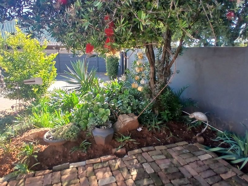 A landscaped garden area featuring established trees, diverse shrubbery, and brick paving, enclosed by a solid boundary wall.