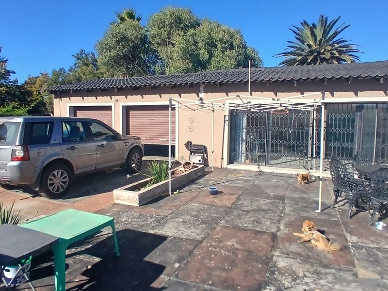 Rear exterior view of the property featuring a paved patio area, double garage with roller doors, and security gates on the sliding glass doors.