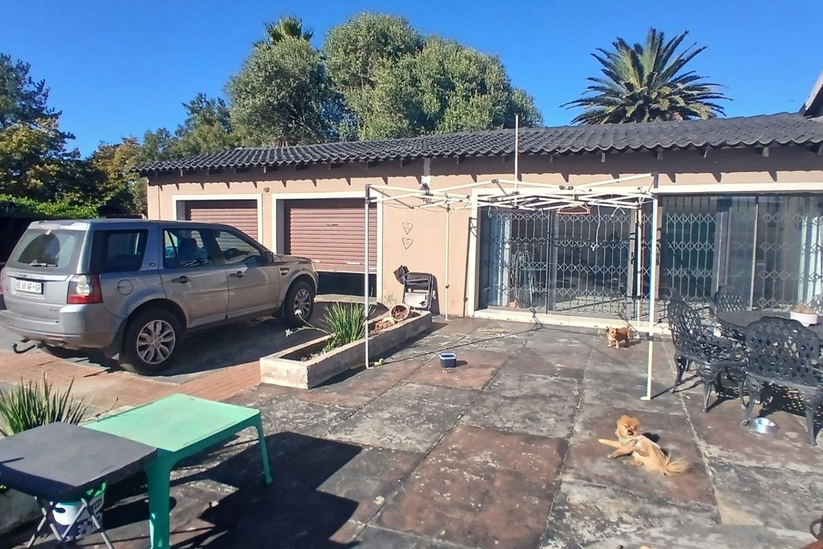 Rear exterior view of the property featuring a paved patio area, double garage with roller doors, and security gates on the sliding glass doors.