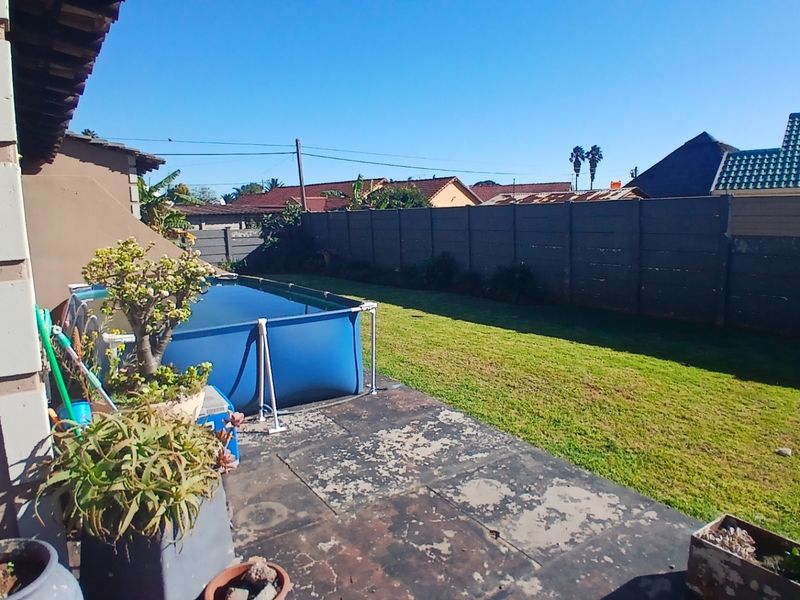 Rear garden area featuring a lawn, a paved patio space, and a precast concrete boundary wall.
